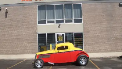 A red and yellow hot rod parked in front of a building.